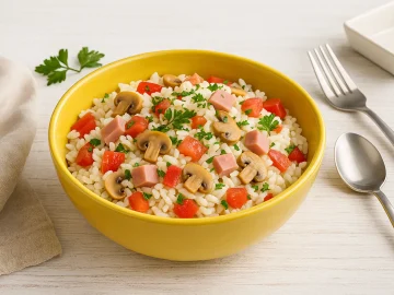 Andalusischer Reissalat mit Gemüse, Schinken und Pilzen in einer gelben Salatschüssel auf weißem Holztisch