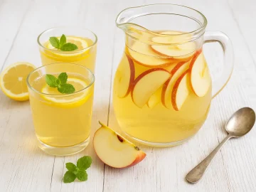 Apfelbowle in Glaskrug mit Weißwein, Sekt und Apfelscheiben auf hellem Holztisch mit Gläsern und Dekoration