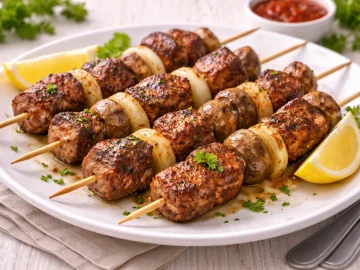 Gegrillte Rindfleischspieße mit Zwiebeln und Champignons auf weißem Teller auf hellem Holztisch