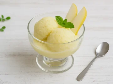 Birneneis cremig serviert in Glasschale mit Birnenspalten und Minze auf Holzhintergrund