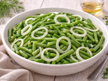 Grüner Bohnensalat mit Zwiebelscheiben und Essig-Öl-Dressing in weißer Schüssel