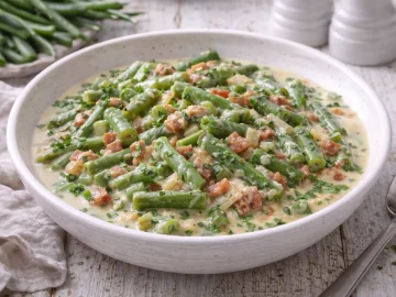 Brechbohnen in Rahm mit Speckwürfeln und Zwiebeln in weißer Schüssel auf weißem Holzhintergrund