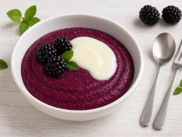 Fruchtige Brombeergrütze im weißen DDR-Dessertteller, serviert mit Sahne und frischen Brombeeren auf weißem Holzhintergrund