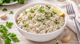 Brotaufstrich aus Räucherfisch in weißer Schüssel mit Petersilie auf hellem Holztisch