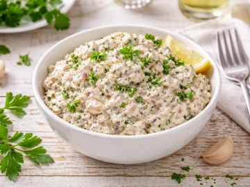 Brotaufstrich aus Räucherfisch in weißer Schüssel mit Petersilie auf hellem Holztisch