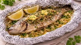 Gegrillter Fisch in Folie mit Kräutern und Zwiebeln serviert