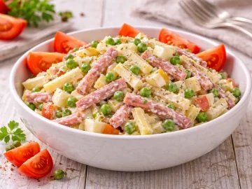 Käse-Wurst-Salat mit Käse, Bierschinken, Apfel und Erbsen in moderner Salatschüssel auf hellem Holztisch