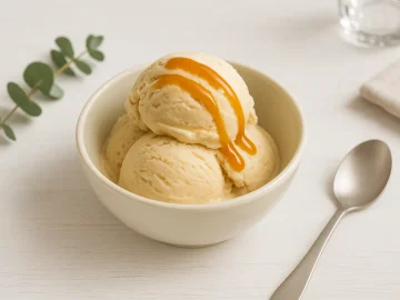 Schale mit cremigem Karameleis, garniert mit Karamellsauce auf weißem Holztisch