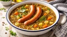 Herzhafte Linsensuppe mit Wiener Würstchen in weißer Emaille-Schüssel auf rustikalem Holztisch angerichtet