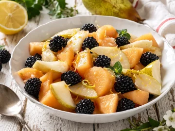 Frischer Melonensalat mit Birnenstücken und Brombeeren in einer weißen Schüssel auf Holztisch