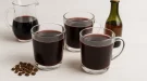 Gläser mit heißem Mokkaglühwein auf weißem Holzhintergrund, dekoriert mit Kaffee, Rotwein und Weinbrand.