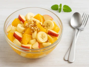 Obstsalat Amor mit Äpfeln, Bananen, Orangen, Ananas und Nüssen in einer Glasschale serviert