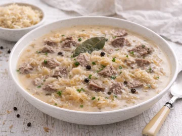 Polnische Krautsuppe mit Sauerkraut und Fleisch in cremiger Brühe in weißer Schüssel auf weißem Holzhintergrund