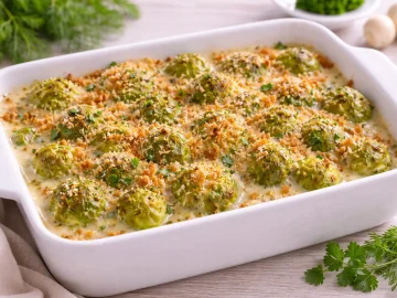 Rosenkohl mit saurer Sahne und knusprigen Semmelbröseln in weißer Auflaufform auf hellem Holztisch