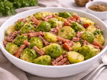 Rosenkohlsalat mit Lachsschinkenstreifen, gewürzter Essig-Öl-Marinade und Kräutern in weißer Schüssel auf hellem Holztisch.