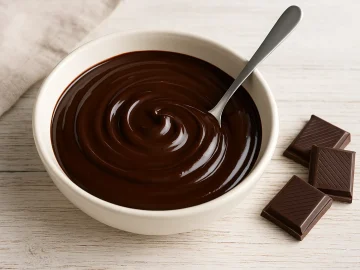 Schokoladenglasur in weißer Schüssel mit Löffel auf hellem Holztisch