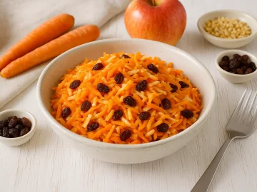 Rustikale weiße Schüssel mit süßer Möhrenfrischkost aus geraspelten Möhren, Äpfeln, Nüssen und Sultaninen auf weißem Holzhintergrund