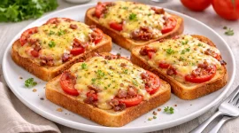 Überbackener Tomatentoast mit Käse und Speck auf einem Teller auf hellem Holzhintergrund