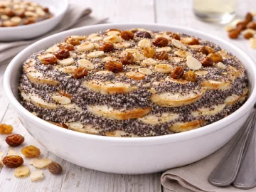 Weiße Schale mit Mohnpielen, geschichteten Semmelstücken und Mohnbrei, dekoriert mit Rosinen und Mandeln auf weißem Holzhintergrund