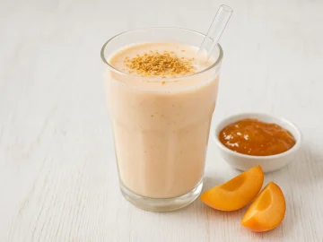 Aprikosenmilch im Glas, bestreut mit Weizenkeimen, auf hellem Holzhintergrund
