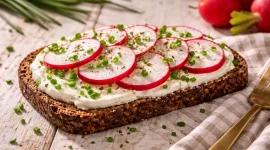 Belegtes Brot mit Frischkäse, Radieschen und Schnittlauch auf Holztisch