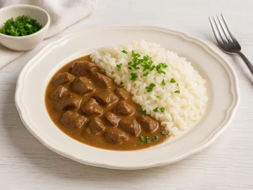 Lebergulasch mit Sauce, Reis und Petersilie auf weißem DDR-Teller mit heller Dekoration