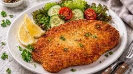 Knusprig paniertes Schnitzel mit Zitronenspalten auf weißem Teller