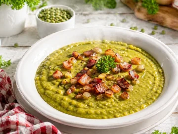 Cremiges Erbsmus in weißer Schüssel mit Speck und Zwiebeln auf rustikalem Holztisch