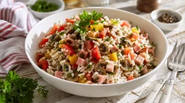 Reissalat mit Schinken, Paprika, Tomaten und Pilzen in weißer Schüssel auf rustikalem Holztisch
