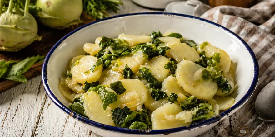 Gedünstete Kohlrabi in einer rustikalen Emaille-Schüssel auf weißem Holztisch mit Küchentuch