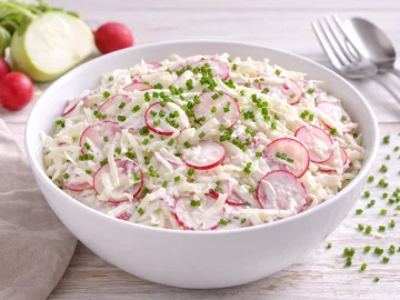 Kohlrabi-Radieschen-Salat mit Joghurt-Dressing und Schnittlauch in einer weißen Salatschüssel auf hellem Holztisch