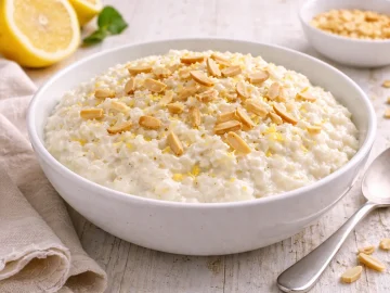 Cremiger Sahnereis mit Mandelstiften in weißer Schüssel auf hellem Holzhintergrund