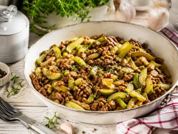 Schmorgurkenpfanne mit Hackfleisch in rustikaler Pfanne auf hellem Holztisch angerichtet