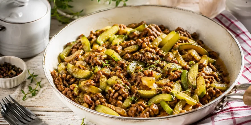 Schmorgurkenpfanne mit Hackfleisch in rustikaler Pfanne auf hellem Holztisch angerichtet