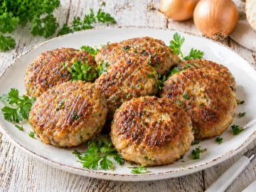 Selleriefrikadellen mit Hackfleisch knusprig gebraten auf weißem Teller mit Kräutern und rustikalem Holztisch