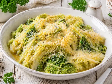 Wirsing mit geschmolzenem Käse und Butter in einer weißen Schüssel auf rustikalem Holztisch angerichtet