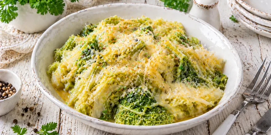 Wirsing mit geschmolzenem Käse und Butter in einer weißen Schüssel auf rustikalem Holztisch angerichtet