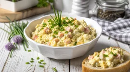 Cremiger Eieraufstrich mit Schinken und Schnittlauch in weißer Schüssel auf rustikalem Holztisch angerichtet