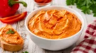 Cremiger Paprika-Aufstrich in weißer Schüssel auf rustikalem Holztisch angerichtet