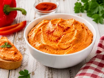 Cremiger Paprika-Aufstrich in weißer Schüssel auf rustikalem Holztisch angerichtet