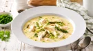 Cremige Hühnersuppe mit Spargelköpfen und zartem Hühnerfleisch in weißem tiefen Teller auf rustikalem Holztisch