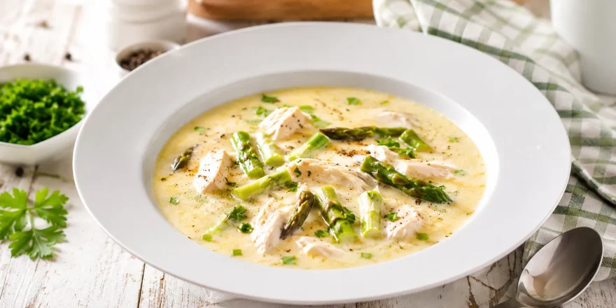 Cremige Hühnersuppe mit Spargelköpfen und zartem Hühnerfleisch in weißem tiefen Teller auf rustikalem Holztisch
