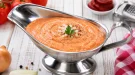 Kalte Tomatensoße in Edelstahlsauciere auf weißem Holztisch angerichtet