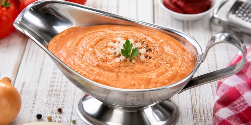 Kalte Tomatensoße in Edelstahlsauciere auf weißem Holztisch angerichtet