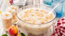 Kinderbowle mit Milch und Pfirsichstücken in Glas auf weißem Holztisch angerichtet