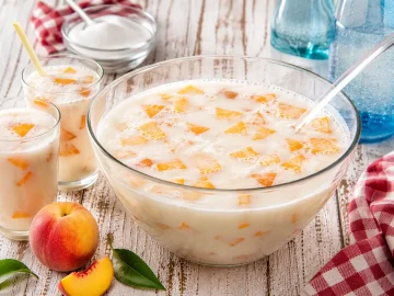 Kinderbowle mit Milch und Pfirsichstücken in Glas auf weißem Holztisch angerichtet