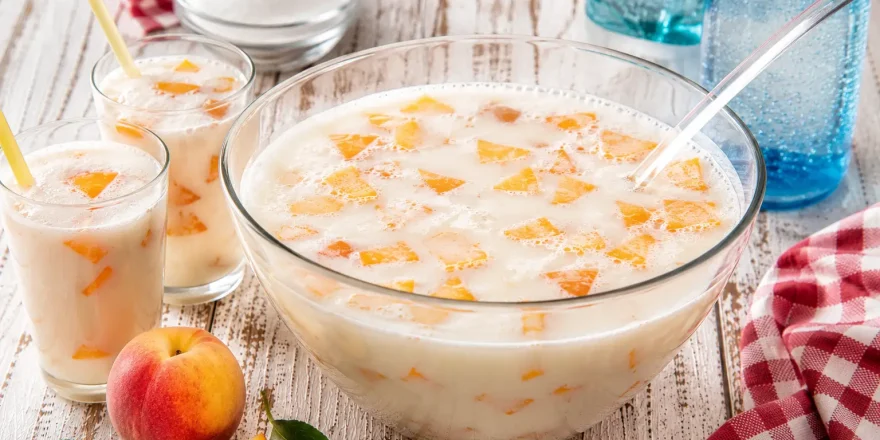 Kinderbowle mit Milch und Pfirsichstücken in Glas auf weißem Holztisch angerichtet