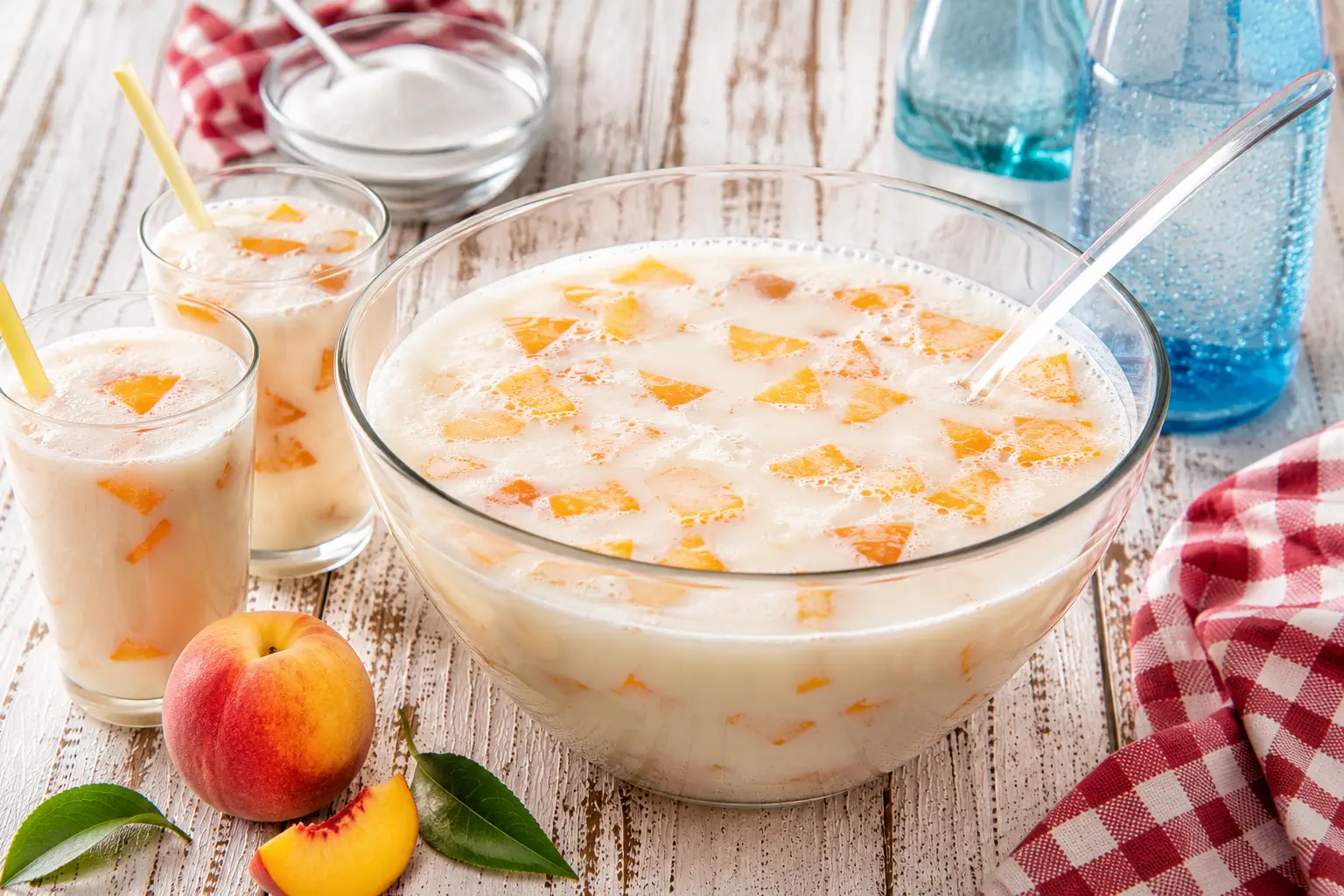 Kinderbowle mit Milch und Pfirsichstücken in Glas auf weißem Holztisch angerichtet
