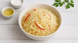 Sauerkrautsalat mit Apfel und Zwiebel in heller Schale auf weißem Holzhintergrund