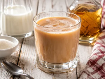 Tee-Mix mit Milch und Rum in Glas auf weißem Holztisch angerichtet